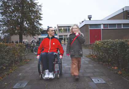 Foto van een vader in een rolstoel zijn dochter van school ophaalt
