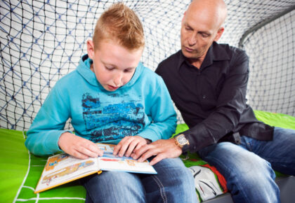 Foto van een vader en zoon op de rand van het bed samen een boeklezen